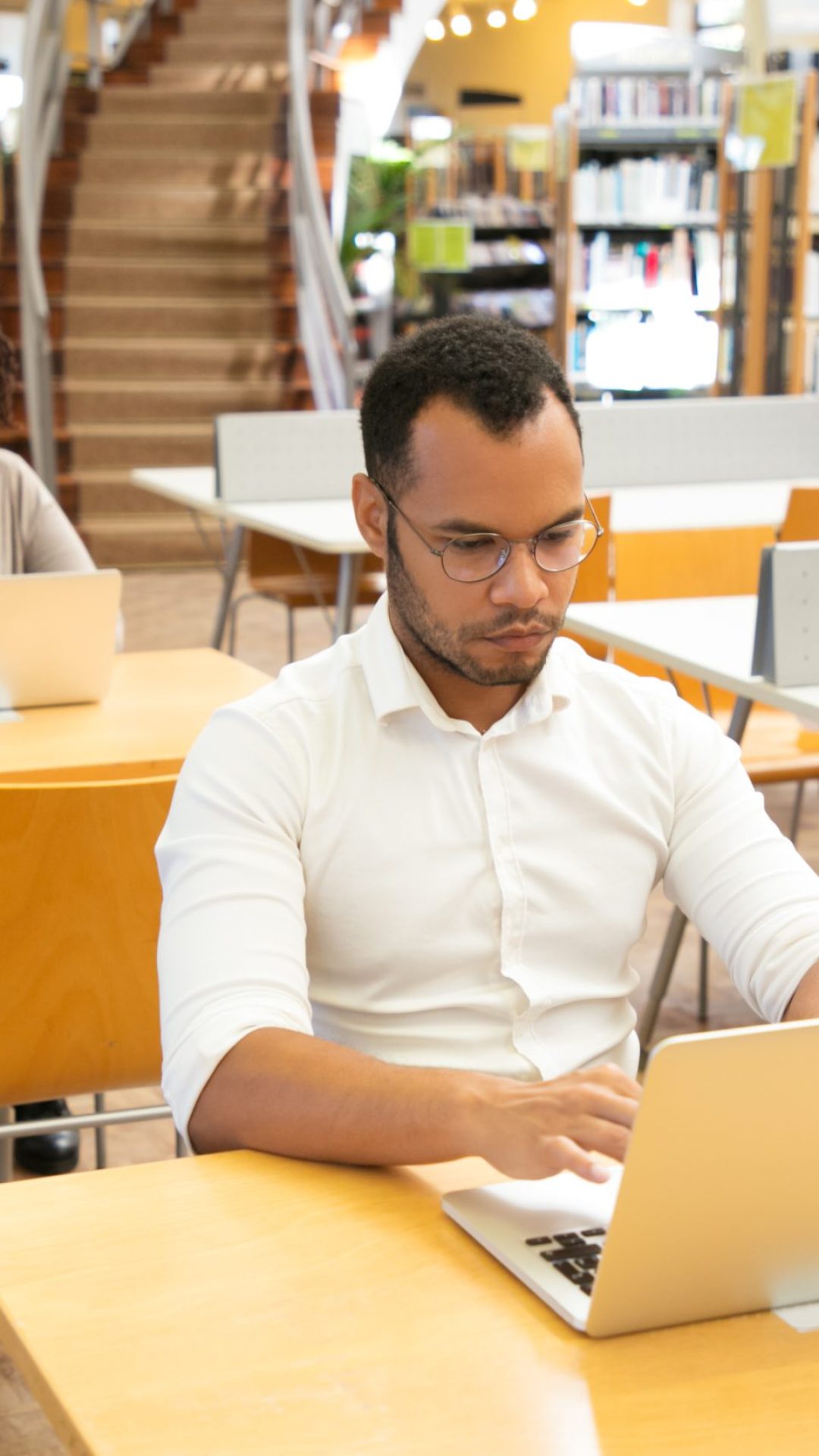 Focused adult students taking online tests in computer class. People sitting at desks and using laptops in library. Education concept
